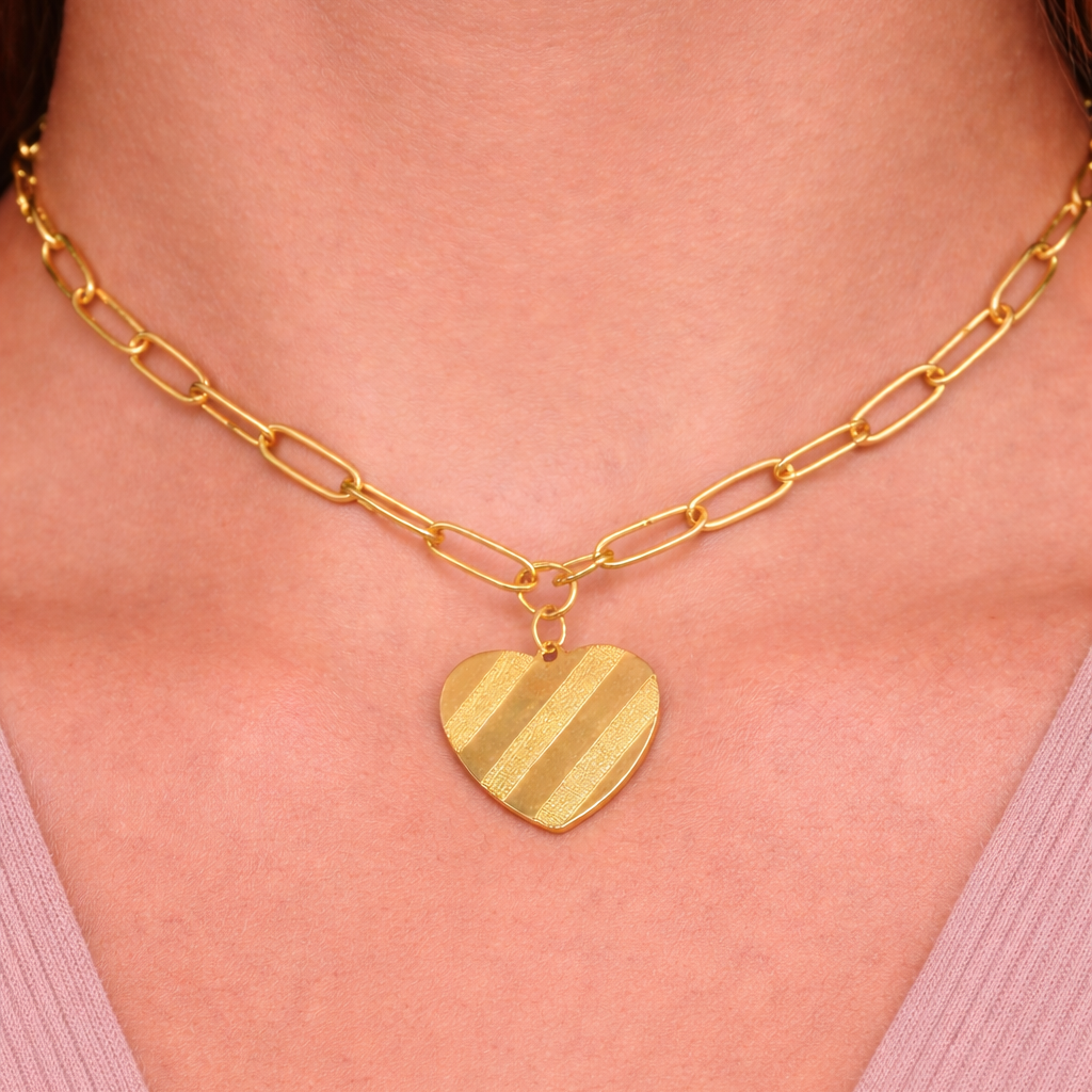 Gold heart-shaped pendant necklace on a person wearing a pink top.