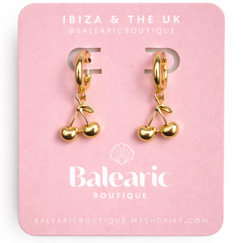Gold cherry-shaped earrings on a pink card with 'Balearic Boutique' branding.