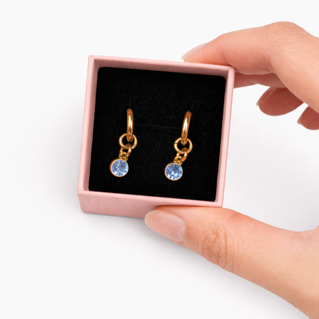 Gold earrings with blue stones in a pink box held by a hand on a white background