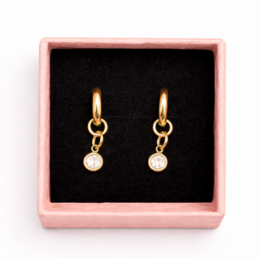Gold hoop earrings with small round charms in a pink box on a white background