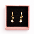 Gold hoop earrings with small round charms in a pink box on a white background