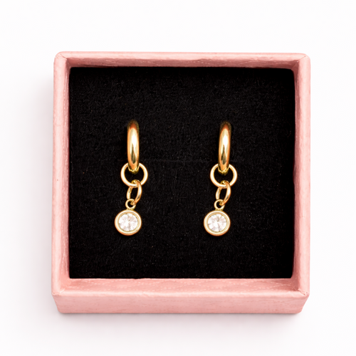 Gold hoop earrings with small round charms in a pink box on a white background