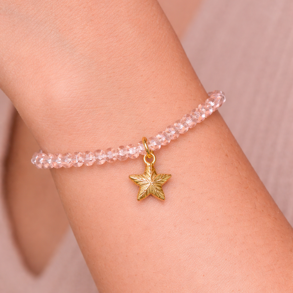 Pink beaded bracelet with a gold star charm on a wrist against a neutral background