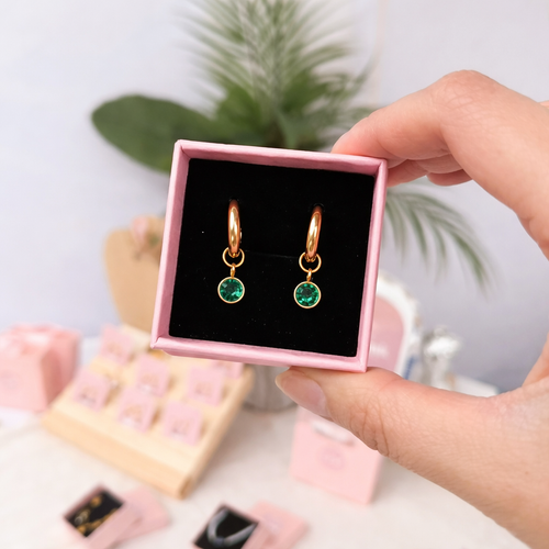 Gold earrings with green gemstones in a pink box held by a hand.