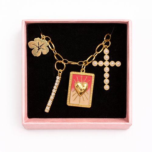 Necklace with charms including a cross, heart, and book design in a pink box on a white background
