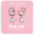 Pair of silver hoop earrings with star charms on a pink card from Balenarc Boutique.