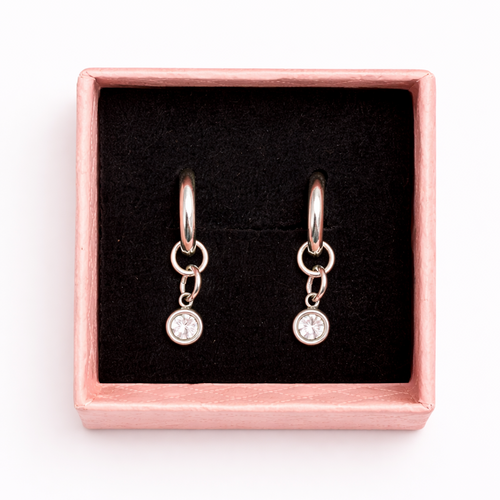 Pair of earrings with clear stones in a pink box on a white background