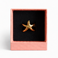 Gold starfish-shaped ring in a pink box on a white background