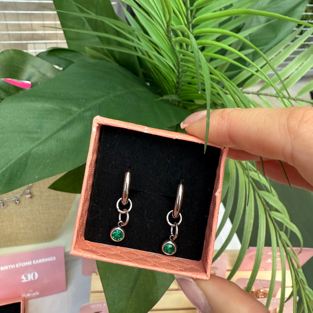 Earrings in a pink box held by a hand with a plant in the background