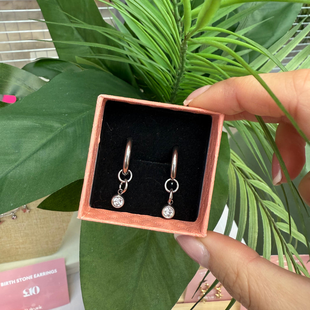 Earrings in a box held by a hand with green plants in the background