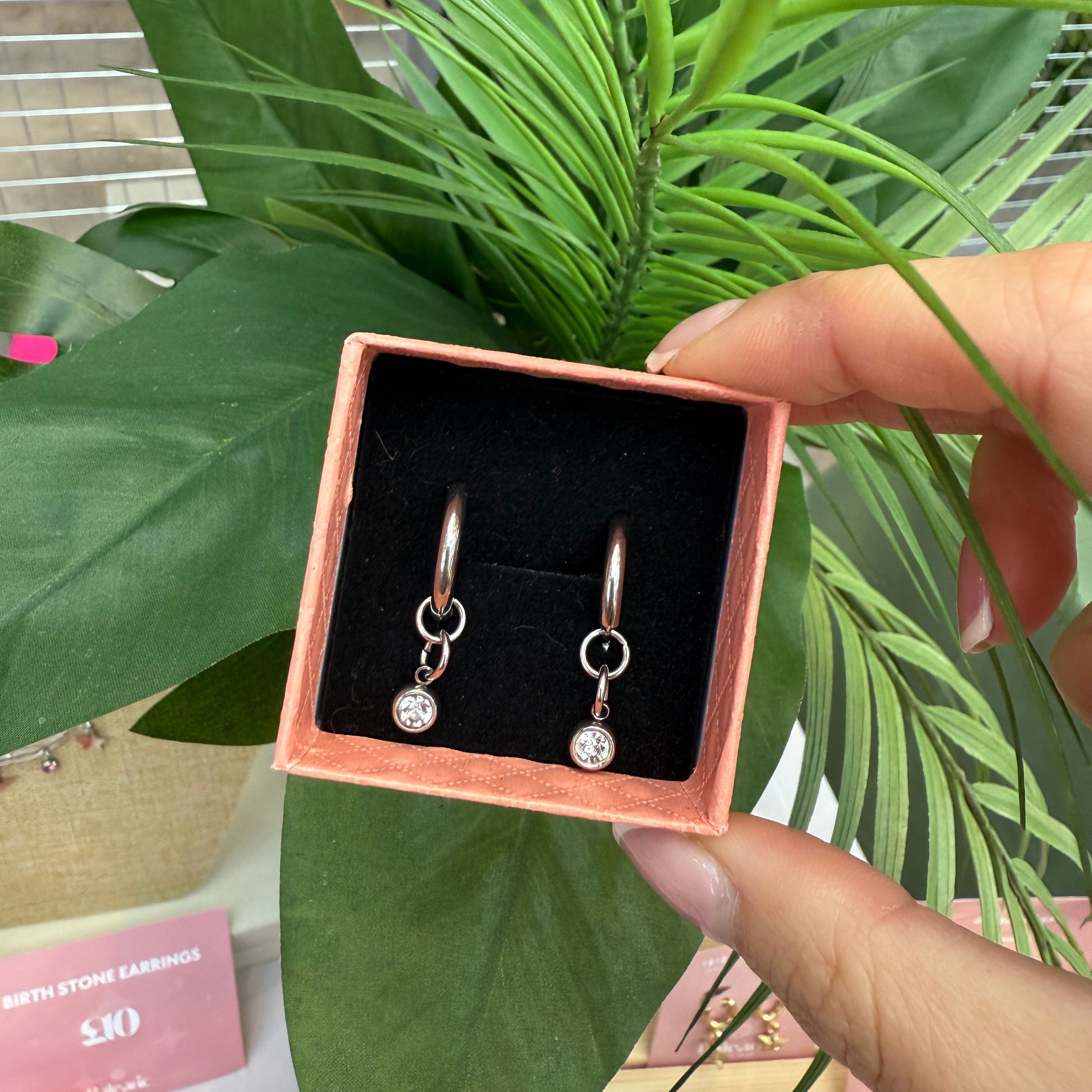 Earrings in a box held by a hand with green plants in the background