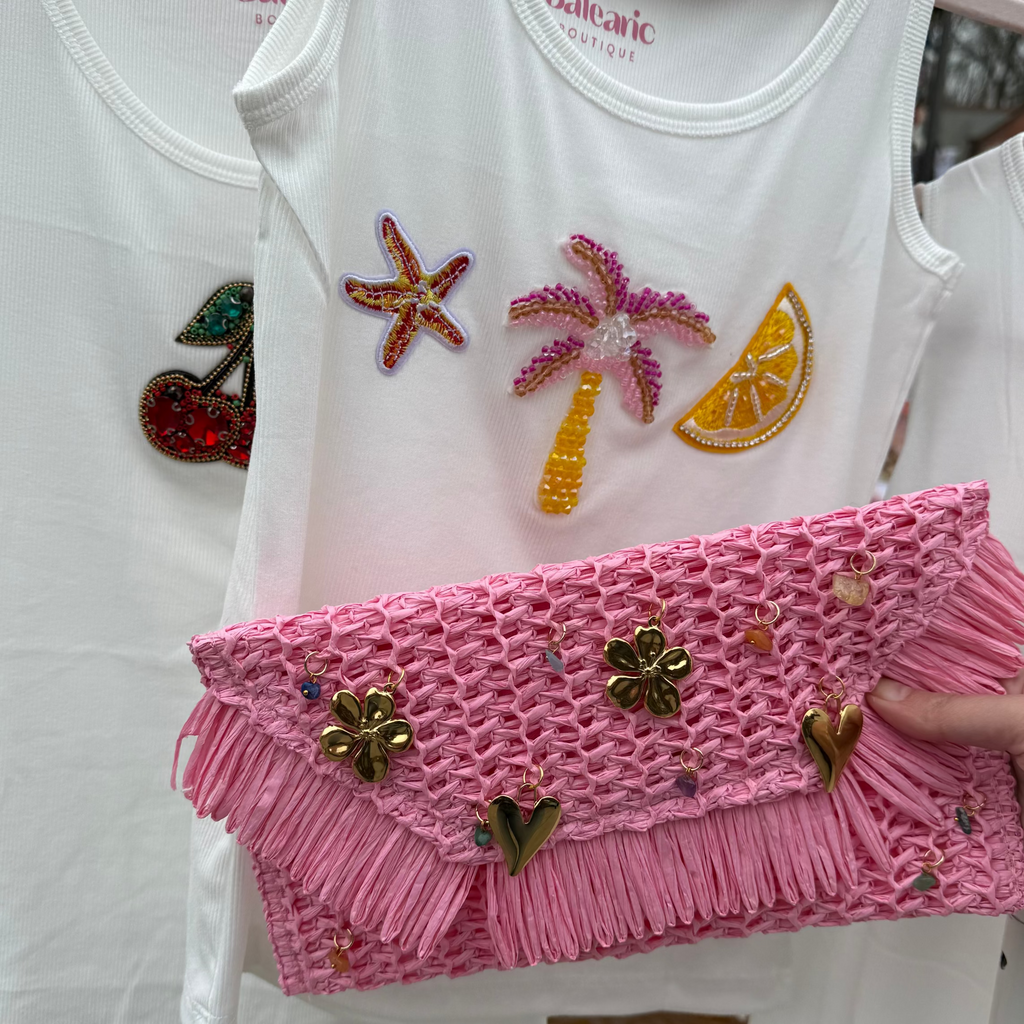 White tank top with colorful embellishments on a hanger, held by a hand.
