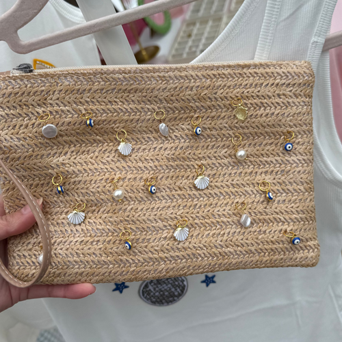 Handheld woven clutch with embellishments in front of a white tank top on a hanger.