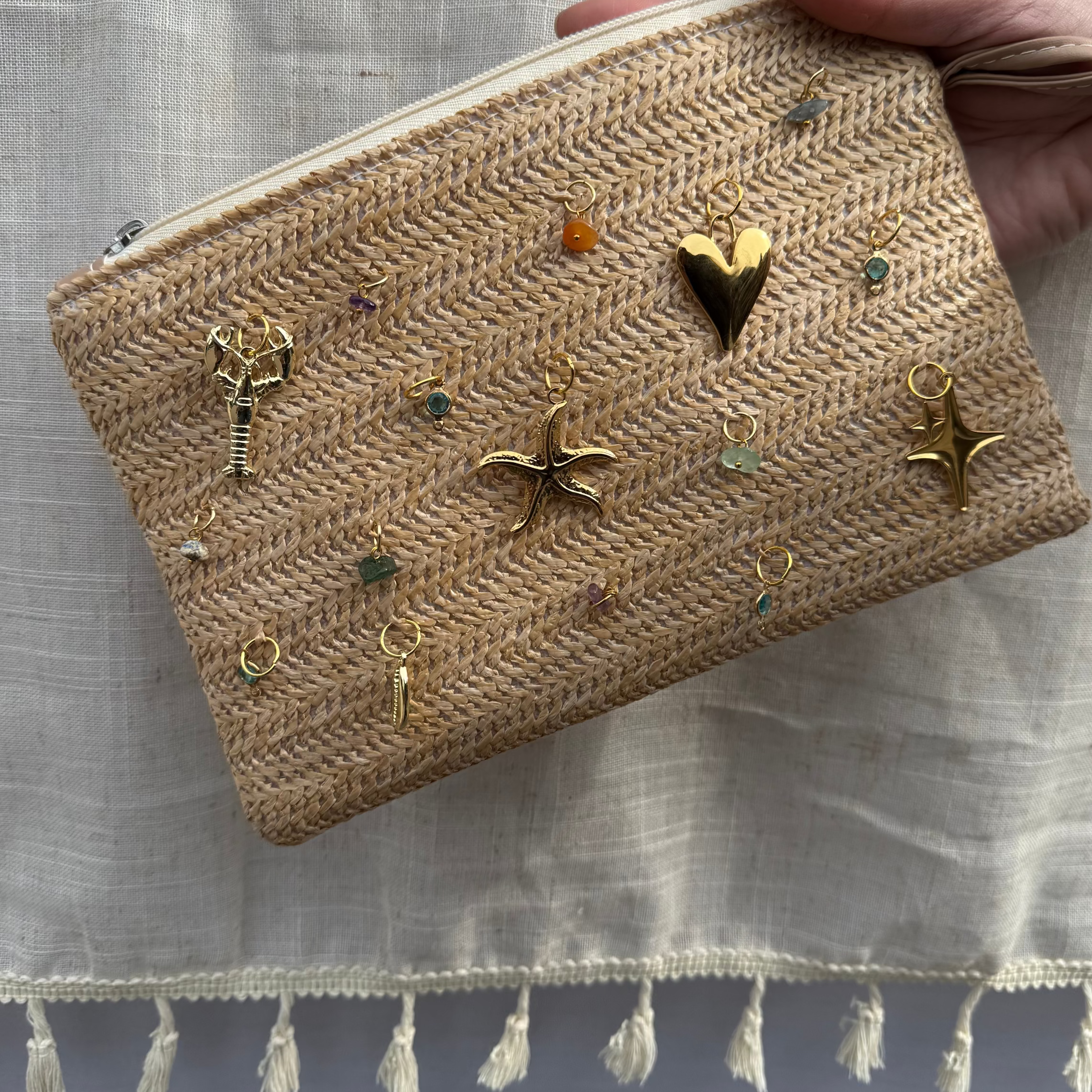 Handheld woven pouch with decorative charms on a light fabric background