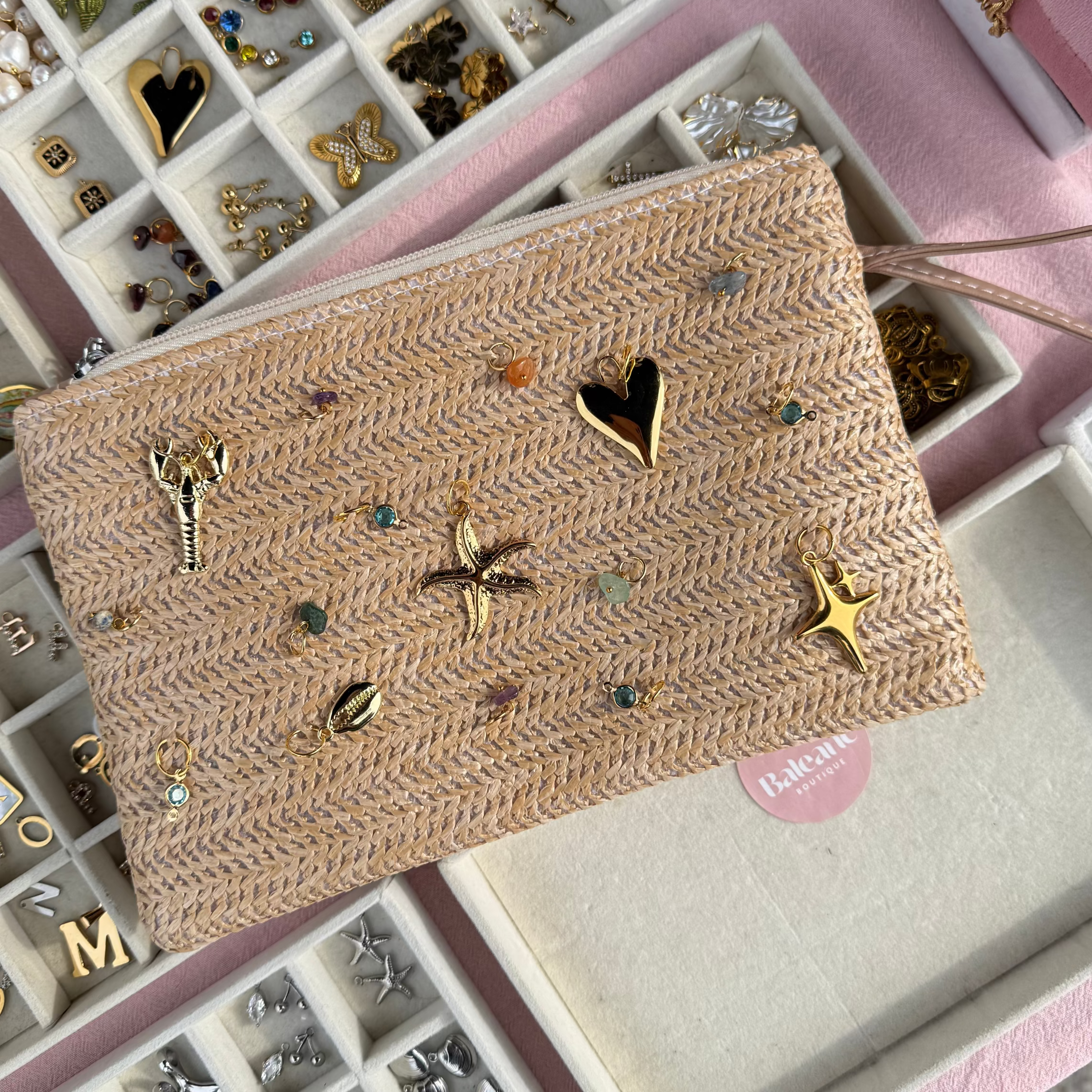 Woven clutch bag with embellishments on a pink surface with jewelry display cases.